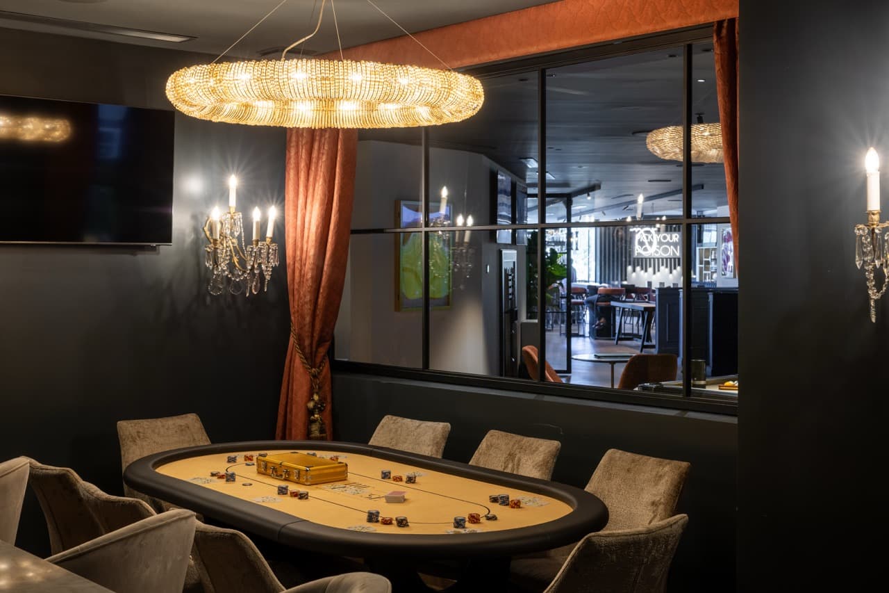 The Laurent-Perrier Players’ Lounge at the Clubhouse Marbella — illuminated champagne walls flank a wood-panelled hearth, Chesterfield armchairs facing in, low tungsten light.