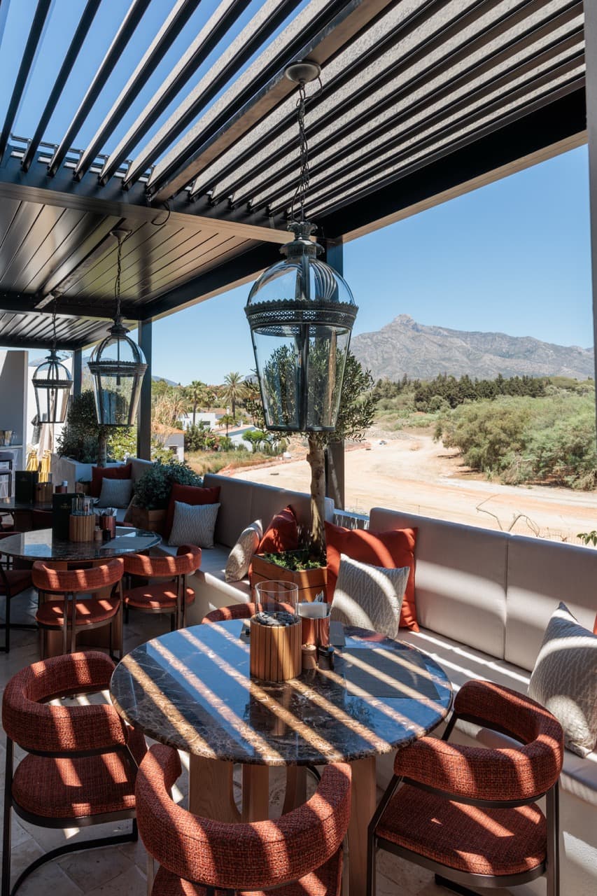 The VIP Terrace at La Sala — pergola roof and pendant lanterns over marble-topped round tables and burgundy chairs, La Concha mountain rising behind.